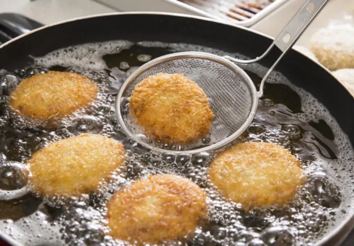 Croquetas doradas friéndose en aceite burbujeante, listas para ser disfrutadas. La bechamel para croquetas se transforma en esta delicia crujiente.