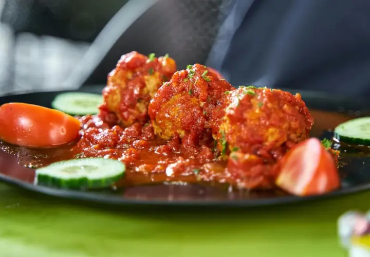 Albondigas con tomate, jugosas y cubiertas de salsa roja, acompañadas de rodajas de pepino y tomate fresco.