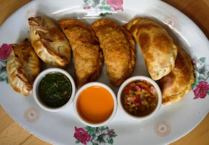Empanadas de carne doradas y crujientes, servidas con tres salsas: chimichurri, picante y criolla.