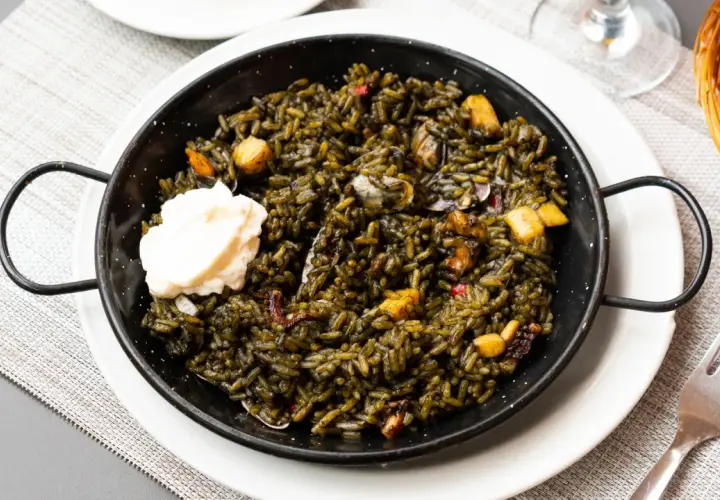 Arroz negro con sepia, un plato de mariscos oscuro y sabroso, servido en una paellera con una cucharada de alioli.