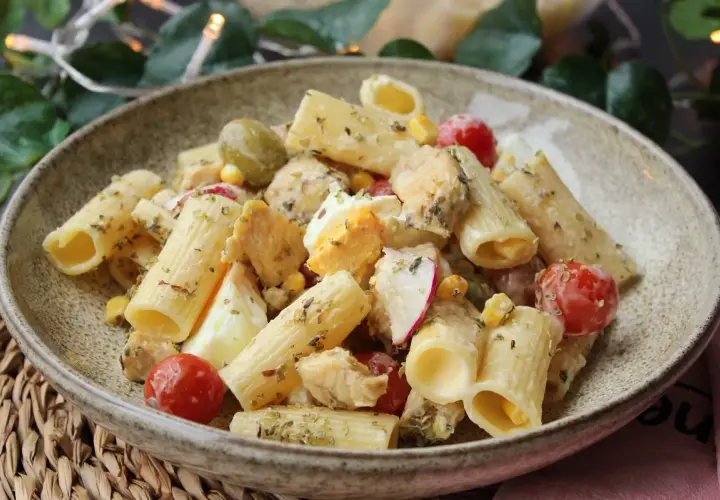 Deliciosa ensalada de pasta con pollo, huevo duro, tomates cherry, aceitunas y maíz, aderezada con hierbas.