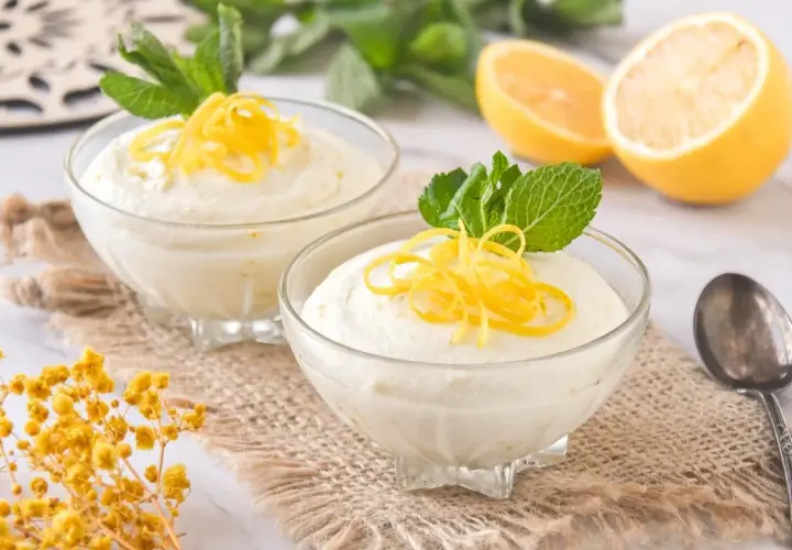 Dos copas de cremoso mousse de limón con leche condensada, decoradas con ralladura de limón y menta.