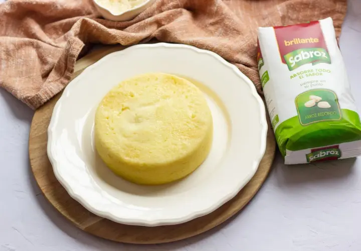 Pastel de arroz amarillo, esponjoso y redondo, servido en plato blanco junto a un paquete de arroz Sabroz.