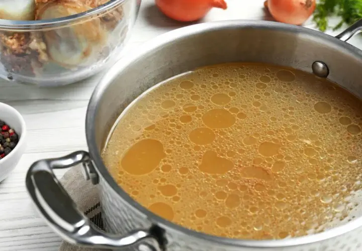 Olla con caldo de huesos burbujeante, junto a un bol con granos de pimienta y laurel, y otro con huesos.