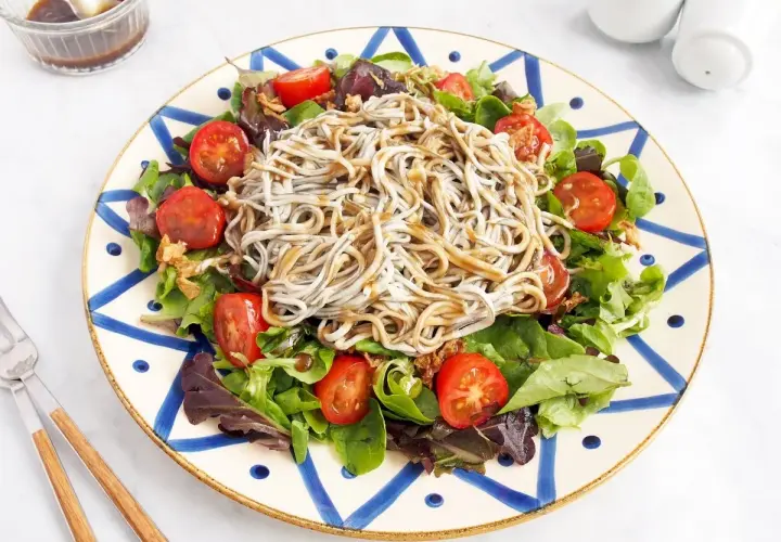 Deliciosa ensalada de gulas con tomates cherry y hojas verdes, servida en un plato decorado.