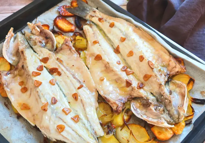 Lubina a la donostiarra recién horneada, con patatas y ajos dorados. Un plato delicioso y fácil de preparar.
