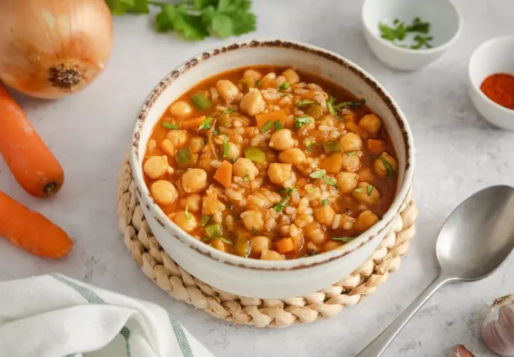 Un reconfortante plato de garbanzos con arroz, zanahorias y pimientos verdes, adornado con perejil fresco.