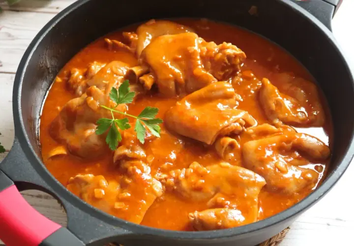 Manitas de cerdo en salsa roja, un plato tradicional español, servido en una sartén negra con perejil fresco.