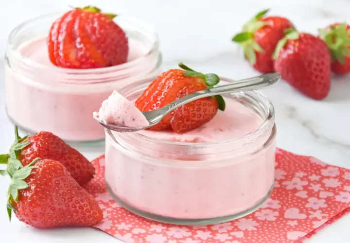 Delicioso mousse de fresa en vasitos, decorado con fresas frescas y una cucharita lista para probar.