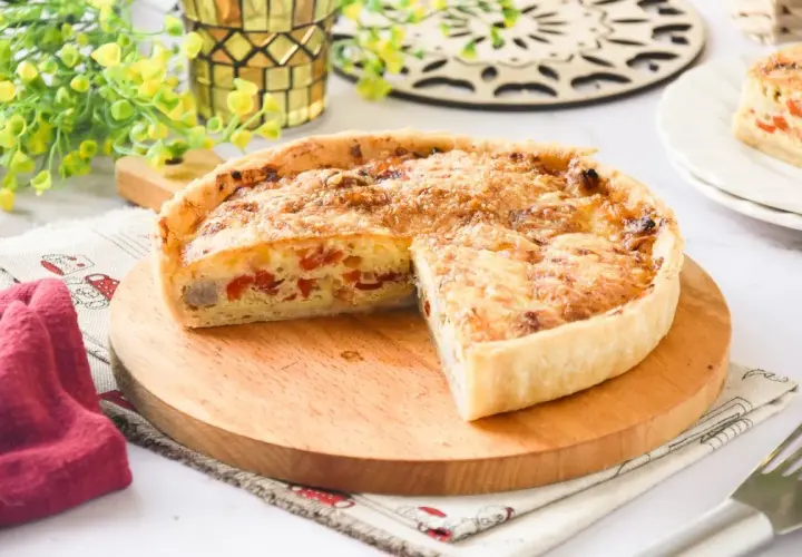 Un delicioso quiche de pollo, con trozos de pimiento rojo y queso gratinado, servido en una tabla de madera.