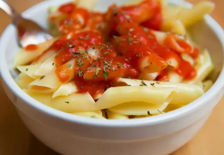 Un tazón de macarrones con tomate y hierbas, listo para disfrutar.