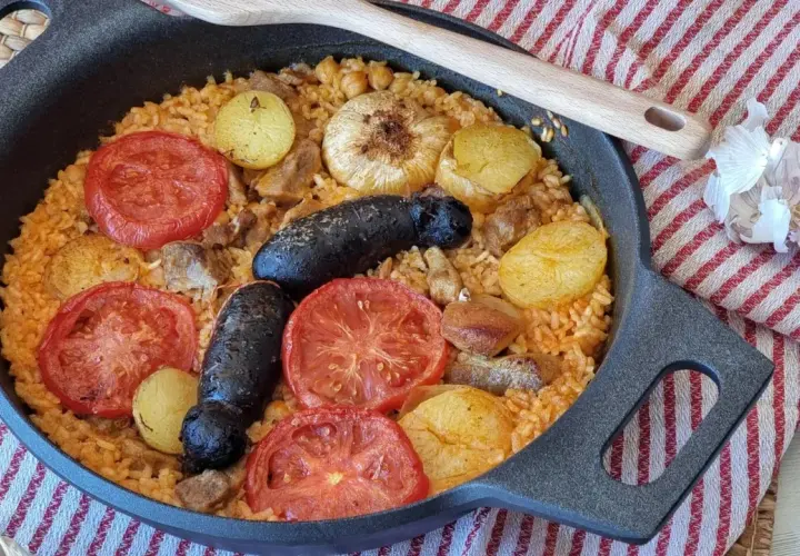 Delicioso arroz al horno con patatas, tomates, morcilla y garbanzos, listo para disfrutar.