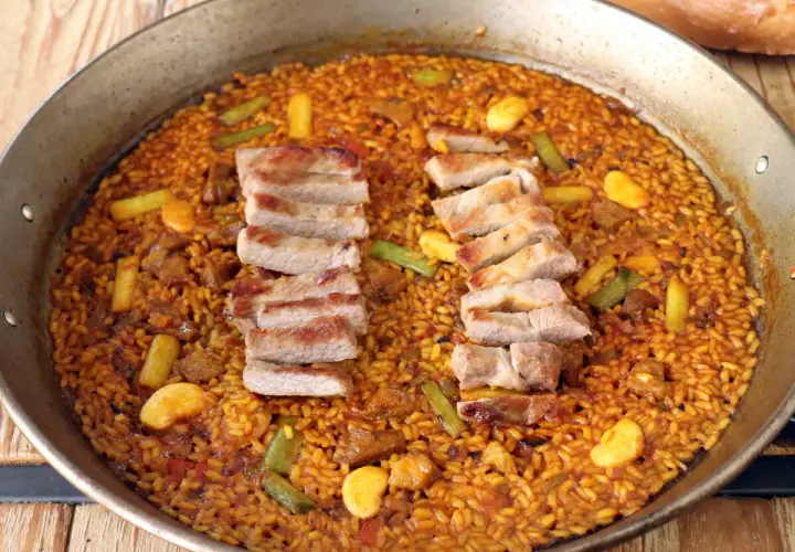 Paella de secreto con trozos de cerdo a la parrilla, judías verdes y trozos de naranja.
