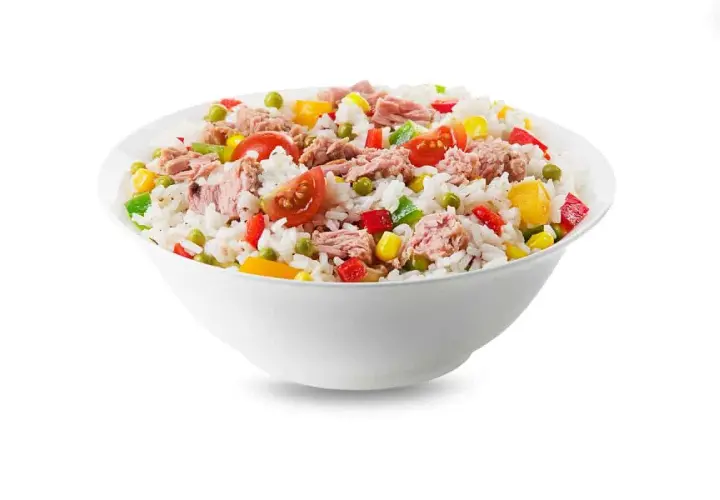 Un tazón blanco lleno de arroz con atún, guisantes, maíz, pimientos y tomates. Una comida fresca y colorida.