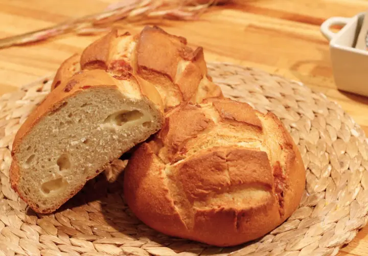 Pan de queso recién horneado, con una miga esponjosa y trozos de queso derretido visibles.