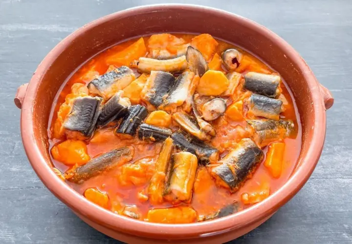 Un cuenco de barro con un sabroso all i pebre, un guiso tradicional de anguilas y patatas en salsa roja.