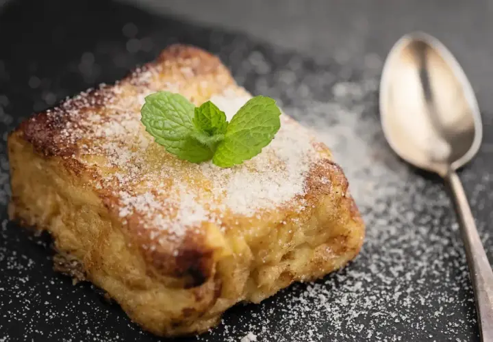 Torrijas con pan brioche, espolvoreadas con azúcar y decoradas con menta. Una cuchara plateada acompaña este delicioso postre.
