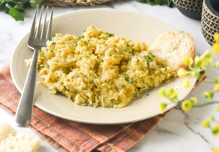 Un plato de bacalao a bras, desmenuzado y mezclado con patatas y perejil, servido con una rebanada de pan.