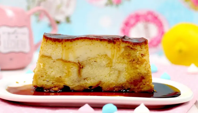 Un trozo de pan de calatrava con caramelo líquido sobre un plato blanco, adornado con merengues de colores y un limón al fondo.