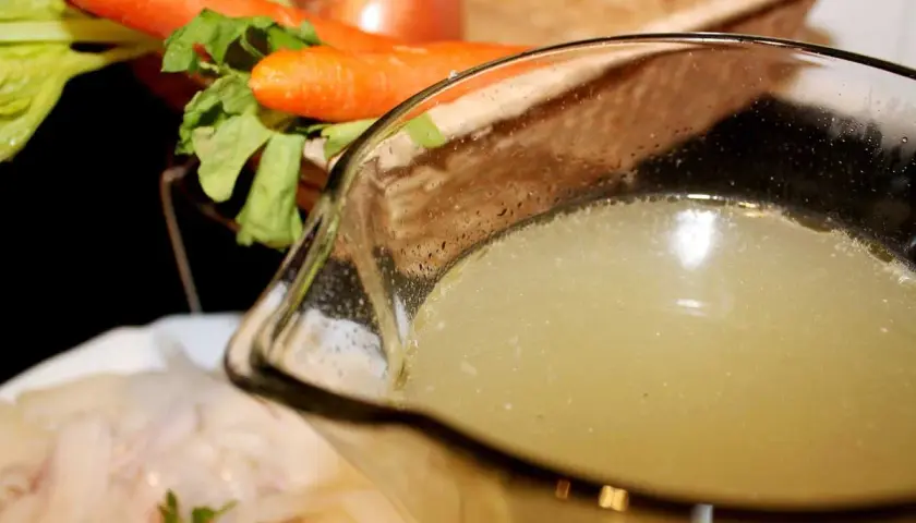 Un delicioso caldo de pescado casero, listo para usar en tu próxima receta. Zanahorias y apio en el fondo.