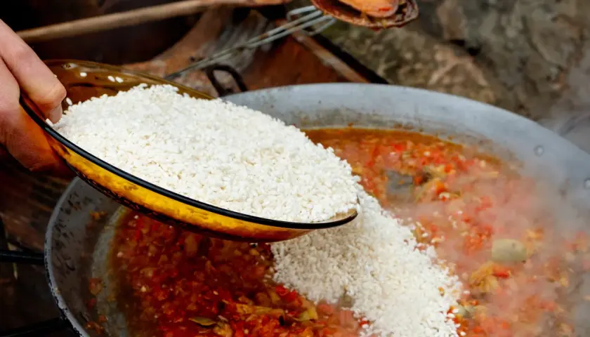 Se añade arroz a una paella de carne burbujeante con verduras rojas y verdes.