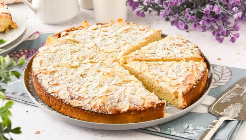 Tarta de almendras dorada, espolvoreada con azúcar glas y almendras laminadas, lista para servir.