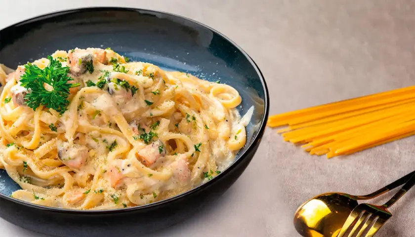 Deliciosa pasta con salmón cremoso, espolvoreada con perejil y queso rallado. Un plato perfecto para disfrutar.