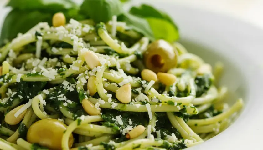 Deliciosa pasta al pesto, con piñones, aceitunas verdes y queso rallado, decorada con hojas de albahaca fresca.