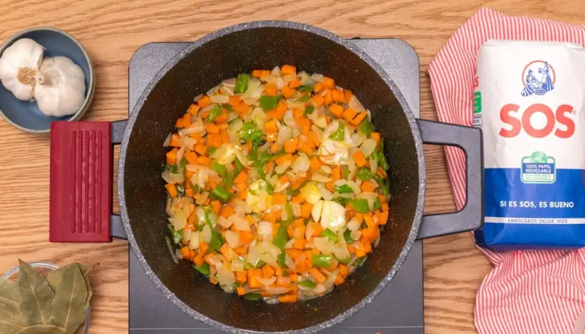 Verduras picadas (zanahoria, pimiento, cebolla) sofriéndose en una olla, listas para añadir lentejas con arroz.
