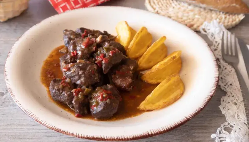 Sabrosa carne de cabra guisada con trozos de pimiento rojo y verde, servida con patatas gajo doradas.