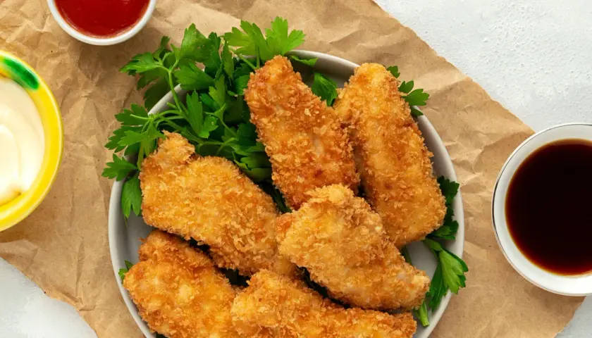Crujientes tiras de pollo empanizadas con panko, servidas con perejil y salsas. El panko es un pan rallado japonés que da una textura extra crujiente.