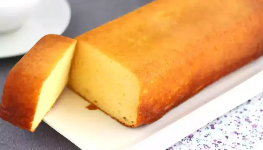 Un delicioso bizcocho de leche condensada, dorado y esponjoso, servido en una bandeja blanca con una porción cortada.