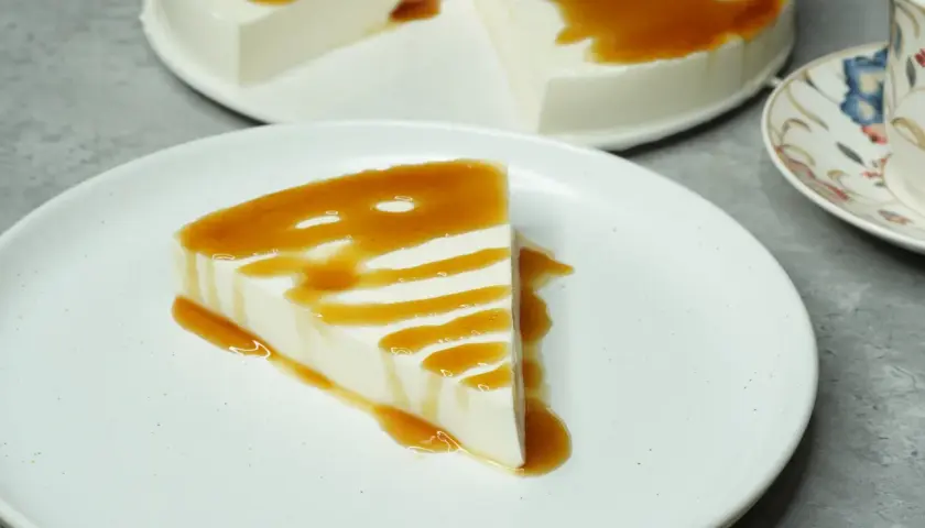Una porción de tarta de cuajada, cremosa y blanca, bañada en un sirope dorado. El postre perfecto para un momento dulce.