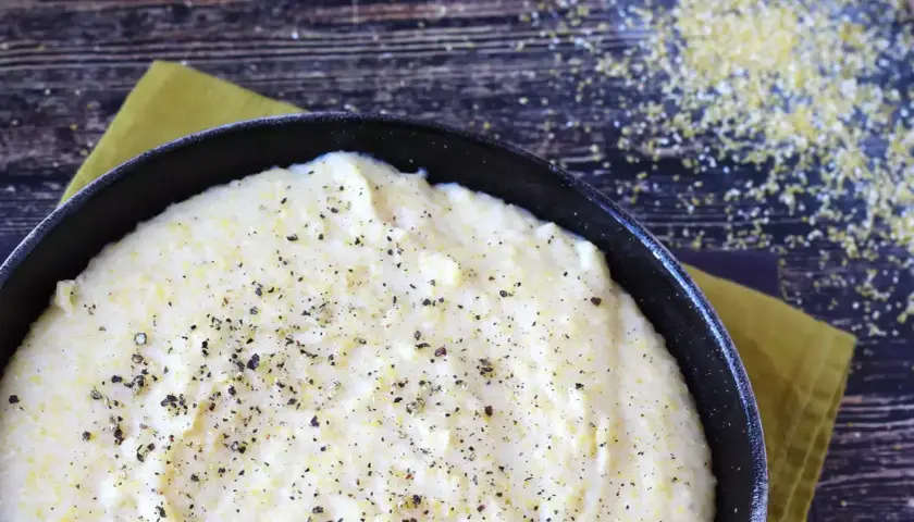 Cremosa polenta que es, servida en sartén negra, espolvoreada con pimienta negra.