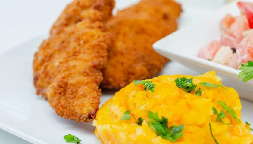 Crujiente solomillo de pollo empanado, puré de zanahoria y ensalada de tomate y cebolla.