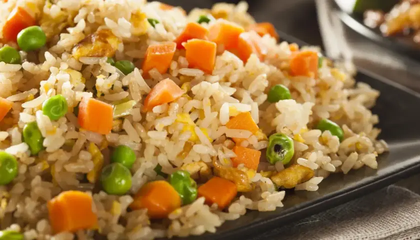 Arroz tres delicias con guisantes verdes, trozos de zanahoria y huevo revuelto, servido en un plato negro.