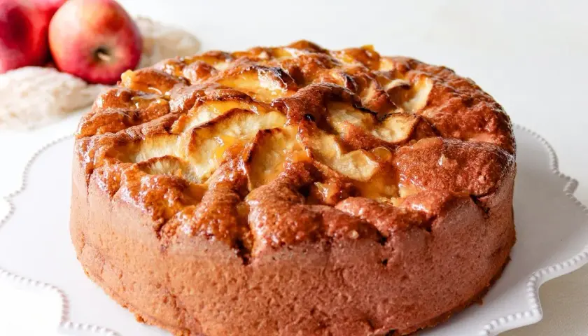 Bizcocho de manzana casero, dorado y jugoso, con trozos de manzana caramelizada en la superficie.