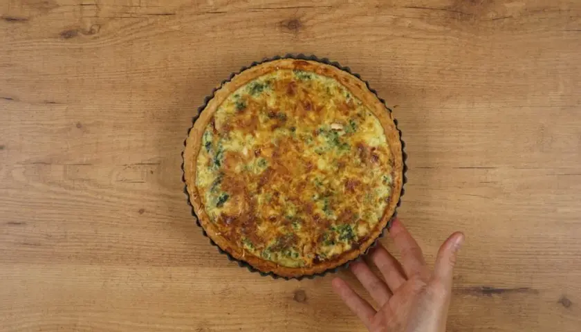 Un delicioso quiche de espinacas recién horneado, con una mano que lo sujeta suavemente.