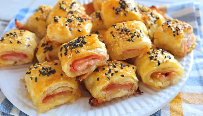 Rollitos de hojaldre jamón y queso, dorados y espolvoreados con semillas de sésamo negro y blanco.