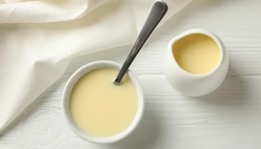 Leche evaporada en un tazón con cuchara y jarra, lista para usar en recetas.