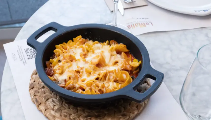 Macarrones al horno gratinados con queso fundido, servidos en una cazuela negra sobre un mantel de mármol.