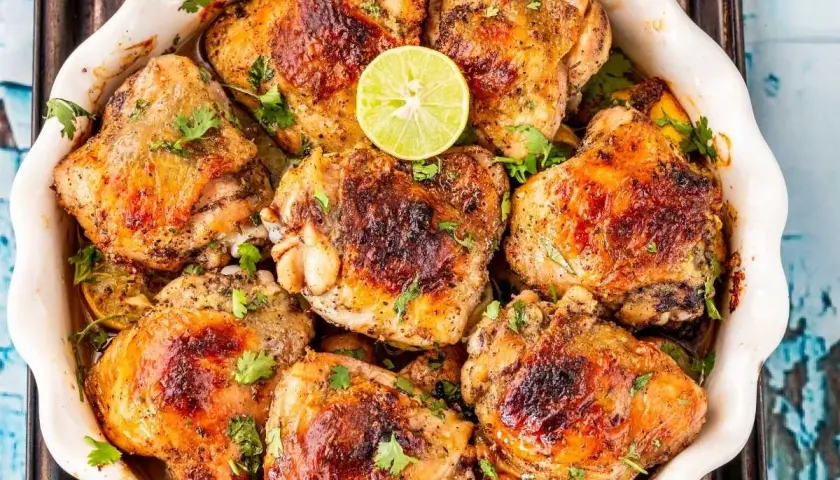 Muslos de pollo dorados y jugosos, horneados con limón y hierbas frescas, listos para servir.