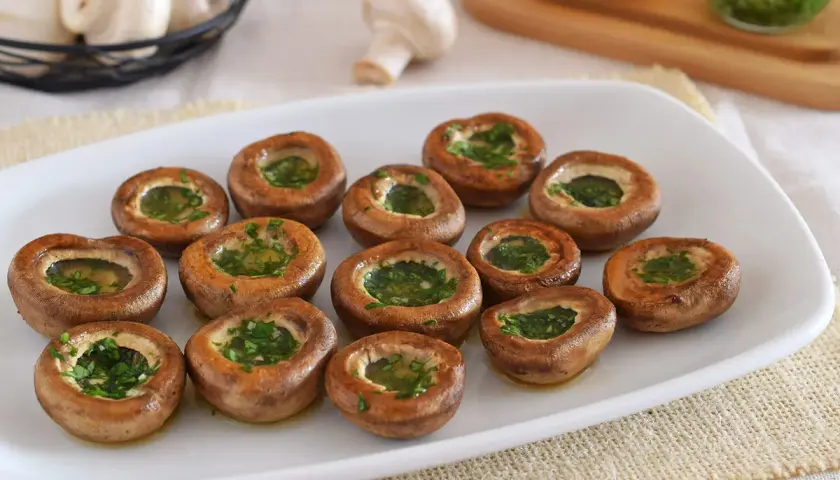Champiñones a la plancha, dorados y rellenos de perejil fresco, listos para disfrutar.