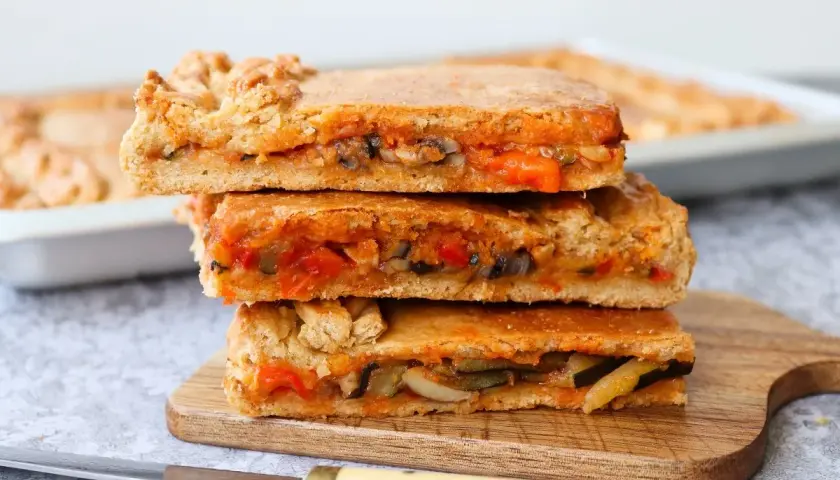 Tres porciones de empanada de verduras apiladas, mostrando el relleno de pimientos, calabacín y tomate.