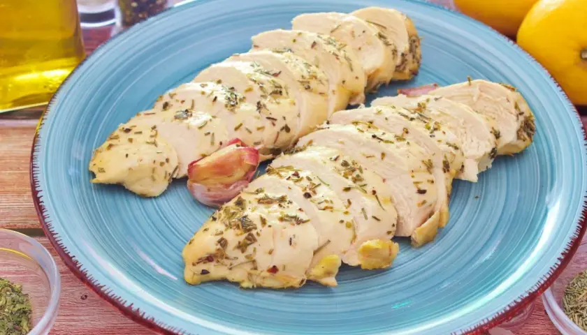 Pechuga de pollo al horno, jugosa y tierna, servida en un plato azul con hierbas aromáticas y ajo.