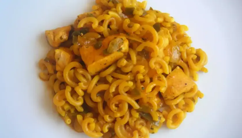 Fideuà de pollo con fideos rizados y trozos de pollo en salsa dorada, servida en plato blanco.