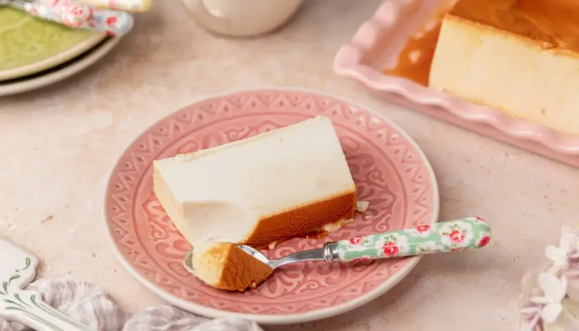 Un trozo de flan de queso cremoso con caramelo dorado, servido en un plato rosa.