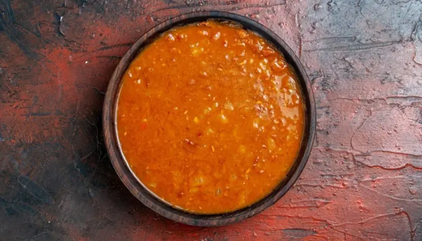 Un tazón de salsa emmy que lleva, con trozos de tomate y especias, sobre una superficie rústica.