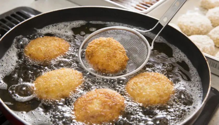 Croquetas doradas friéndose en aceite burbujeante, listas para ser disfrutadas. La bechamel para croquetas se transforma en esta delicia crujiente.