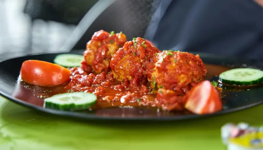 Albondigas con tomate, jugosas y cubiertas de salsa roja, acompañadas de rodajas de pepino y tomate fresco.